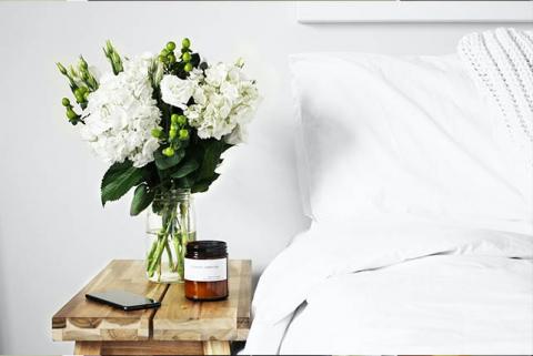 A well made bed next to a bedside table with a vase of flowers
